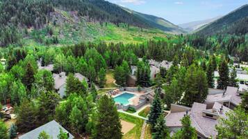 Zona residencial con piscina rodeada de casas, con montañas boscosas al fondo.