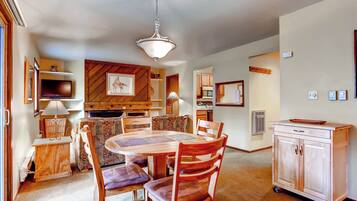 Un comedor con mesa y sillas de madera, televisor y área de cocina con armarios y microondas.