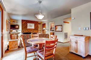 A dining area with a wooden table and chairs, a television, and a kitchen area with cabinets and a microwave.