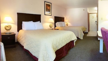 A hotel room with two beds, each with a headboard, bedside lamps, and a framed picture on the wall.
