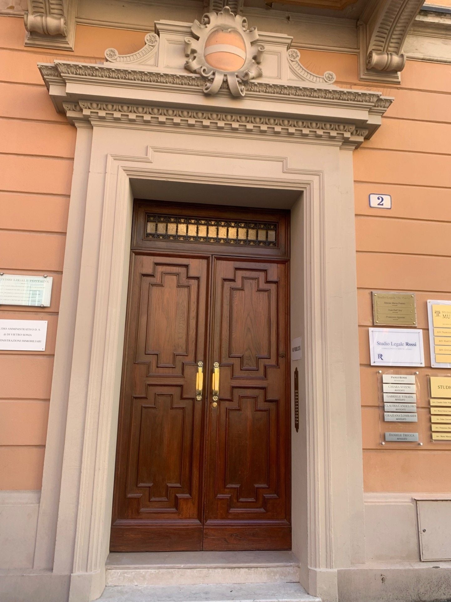 Una doppia porta in legno con architrave decorativo, una targa con il numero '2' e diverse targheggiature di studi legali sulla parete.