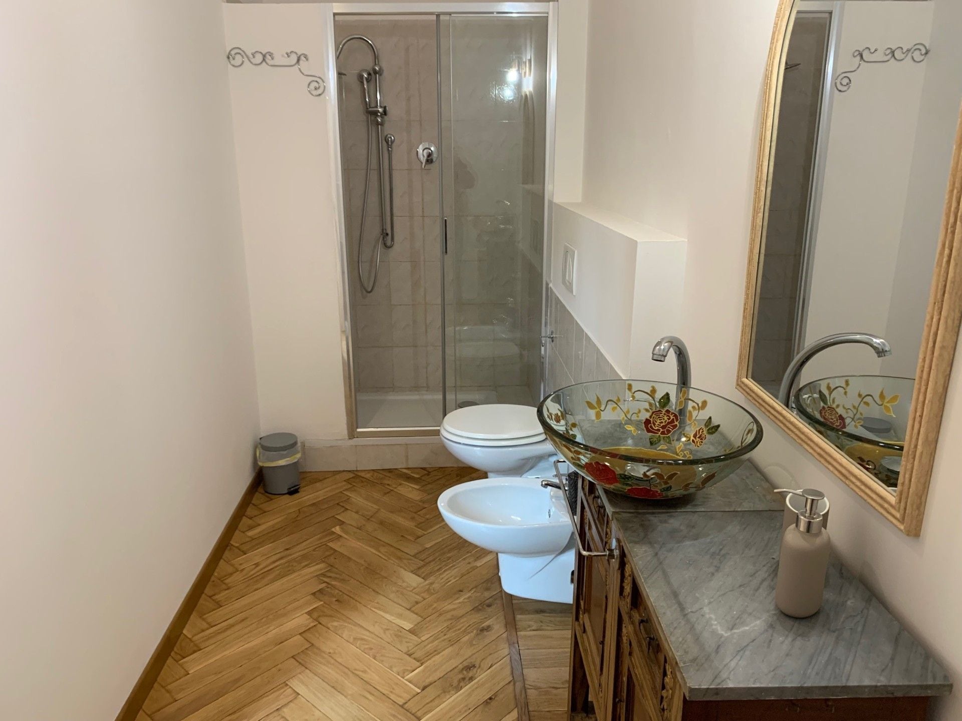 Une salle de bain comprenant une douche à parois de verre, des toilettes, un bidet, un lavabo en verre et un miroir.