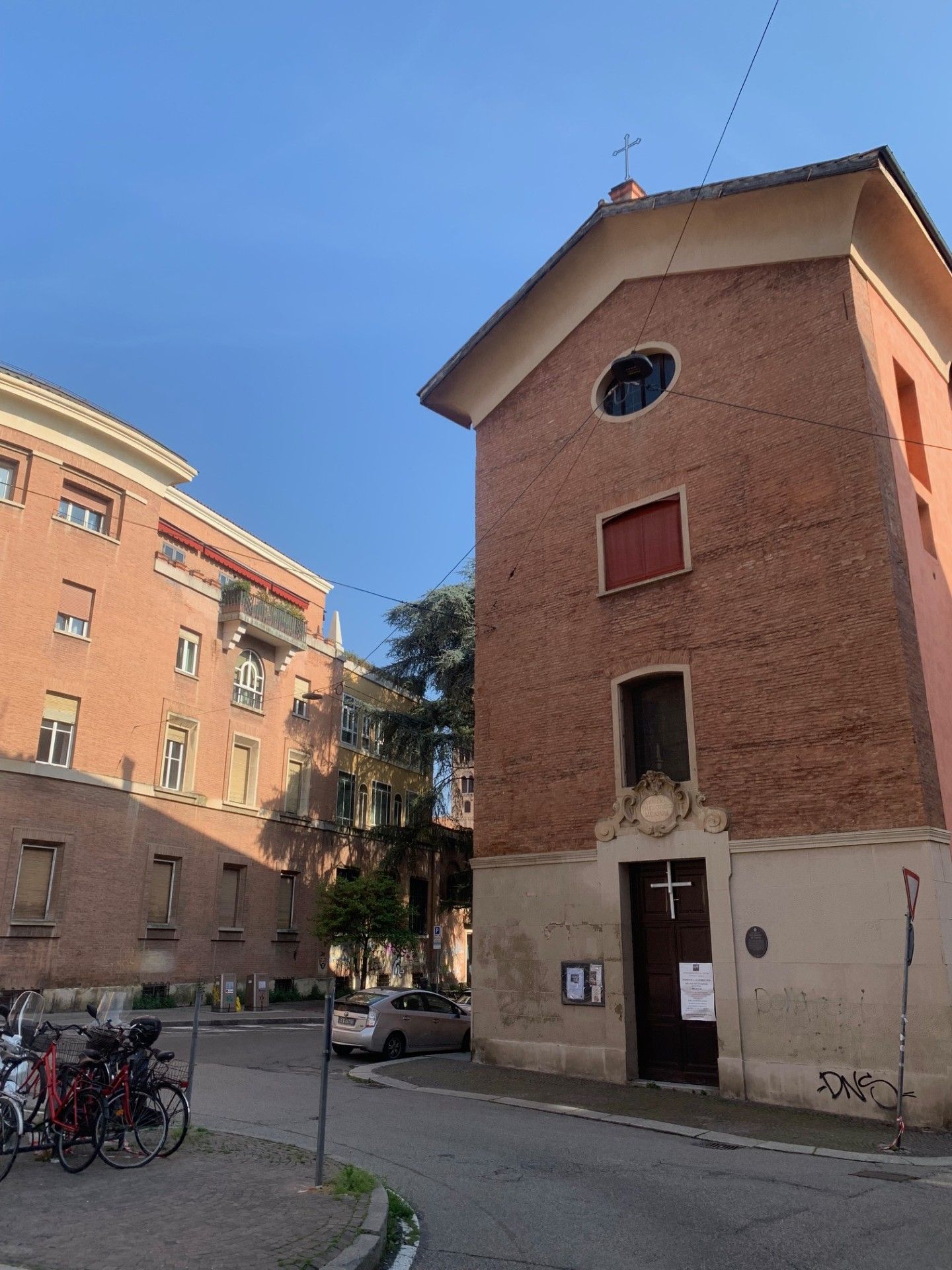 Un bâtiment à deux étages, doté d’une façade en briques rouges, d’une petite fenêtre circulaire et d’une porte surmontée d’une croix.