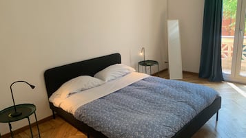 Une chambre à coucher avec un lit, une table de chevet, une lampe et une vue sur l’extérieur.