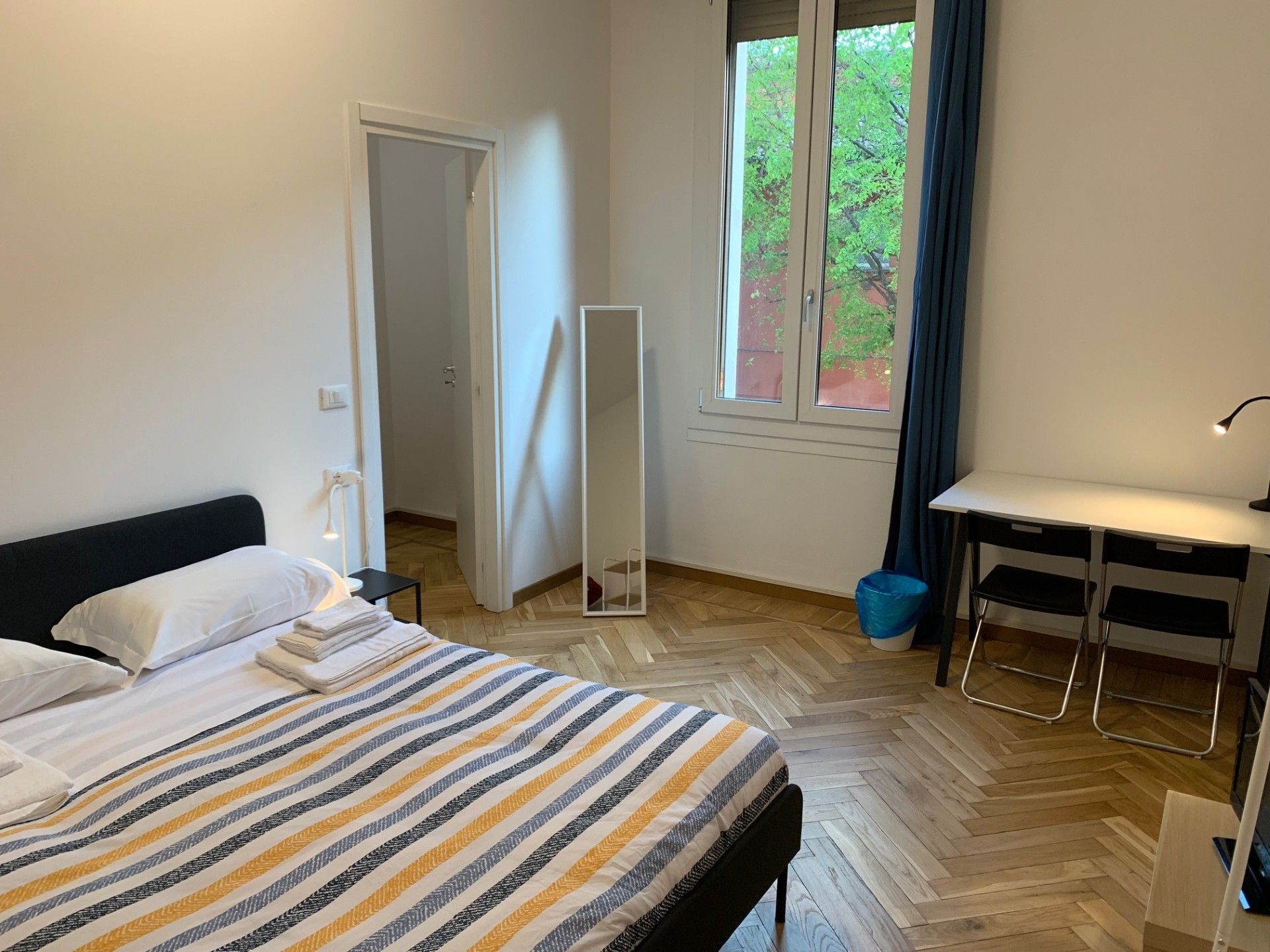 Un dormitorio con cama, escritorio, silla, ventana con vistas y puerta.