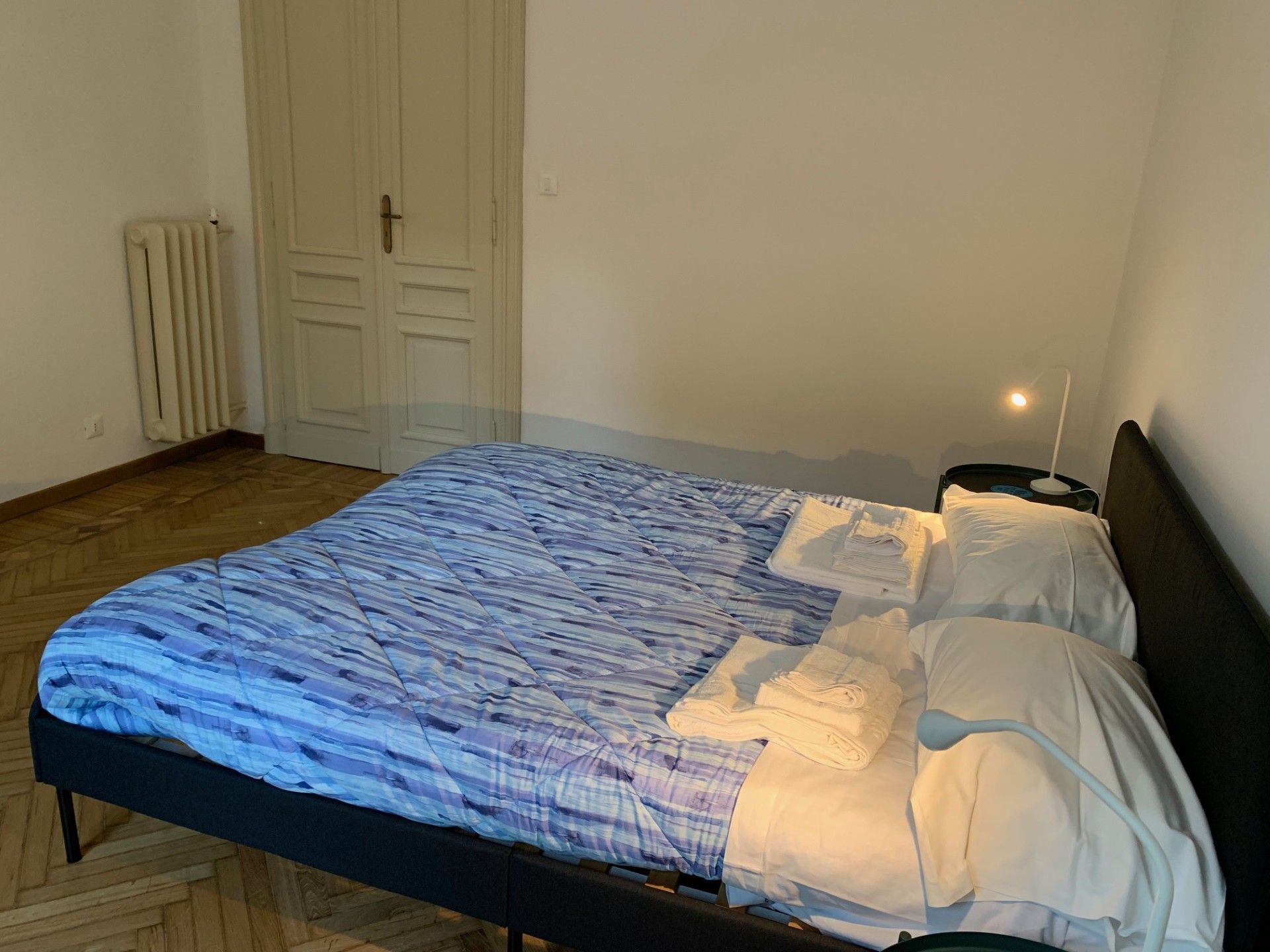 Un letto singolo con una coperta a righe blu e bianche, un cuscino bianco e un comodino con una lampada.