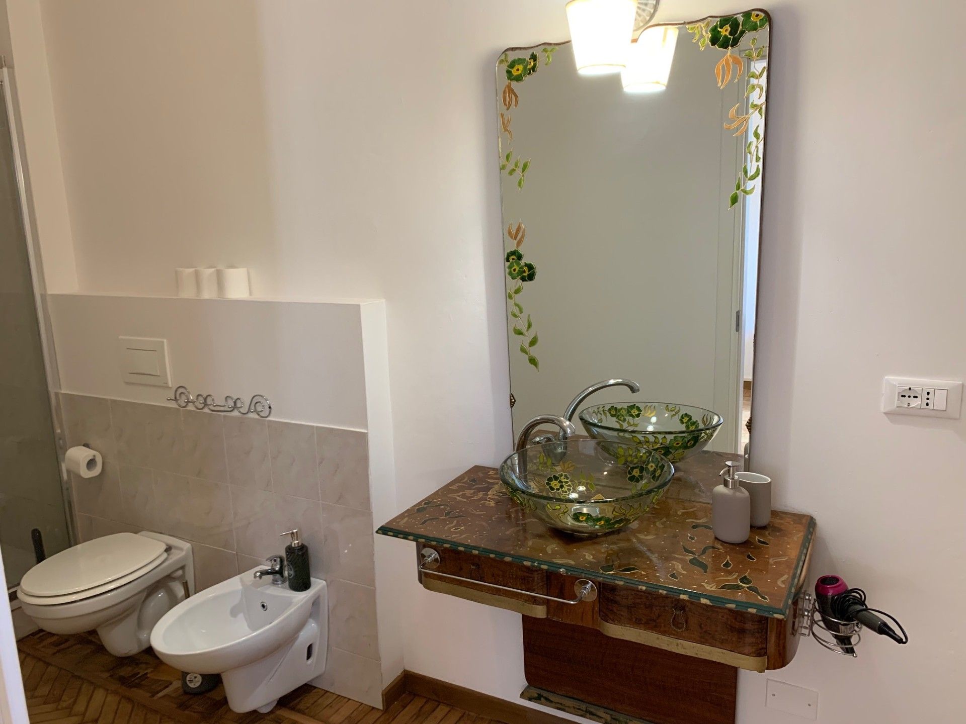 Un bagno con il water, un bidet e un lavabo in vetro decorato con motivi floreali.