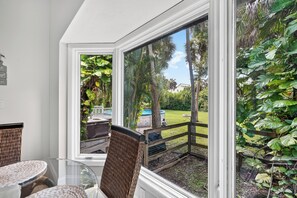 Ein Zimmer mit Glastisch, Korbstühlen und Blick auf einen Garten mit Pool und üppigem Grün.