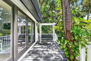A covered outdoor area with a wooden deck, a white pergola, and a glass door leading to an interior space. - Nokomis Beach Tropical Tree House! (Nokomis)