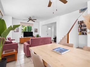Ein modernes Wohnzimmer mit einem Holzesstisch, Sofas, einem Fernseher und einer Treppe, die zu einer Bibliothek führt.