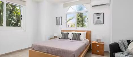 Un dormitorio con cama, mesita de noche, silla y ventana.