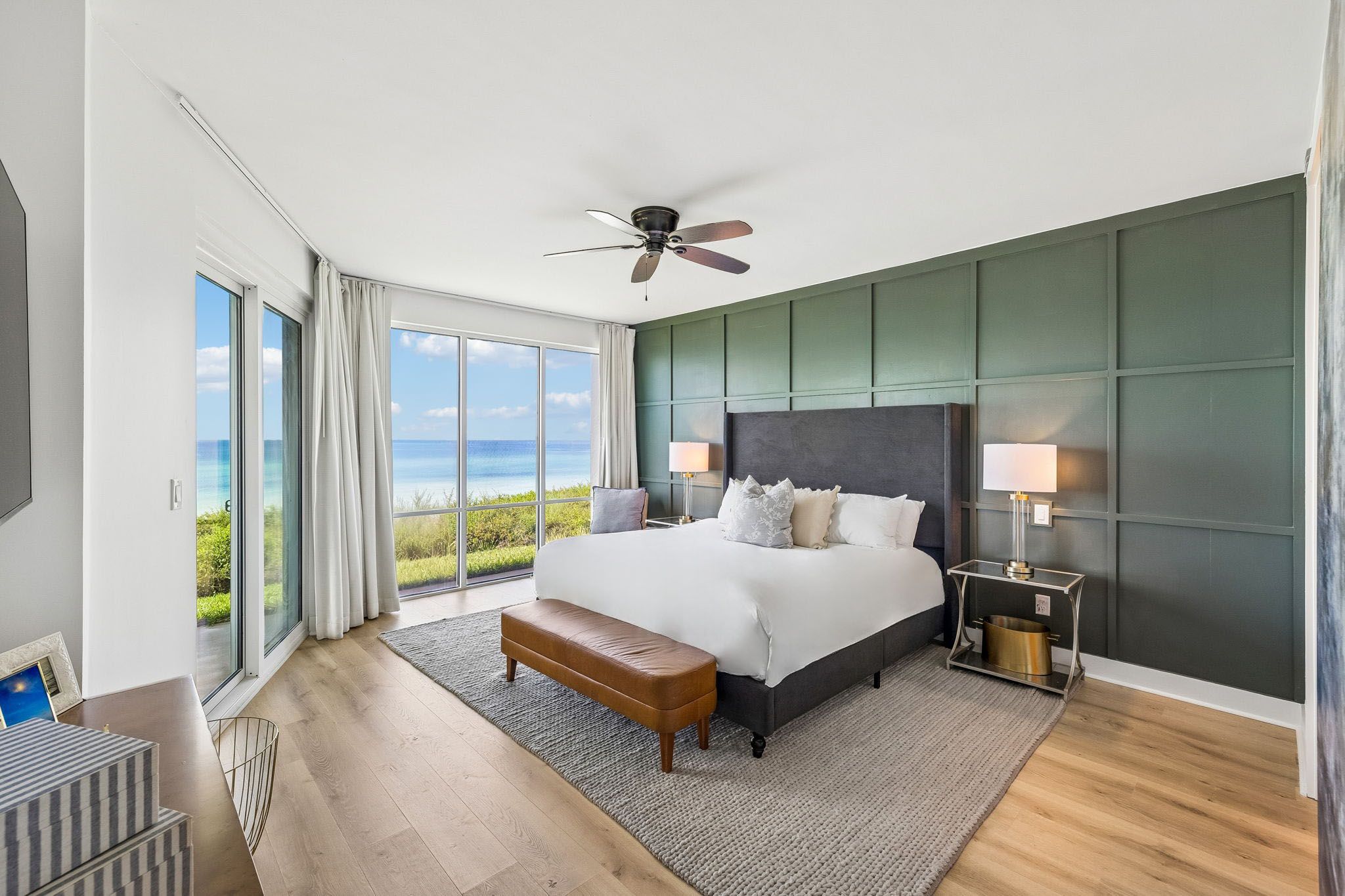 Une chambre moderne avec un grand lit, un ventilateur de plafond, une vue sur l’océan et un balcon.