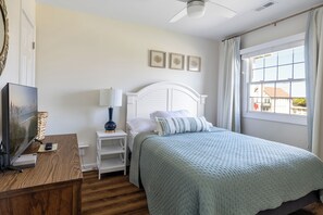 A bedroom with a bed, a bedside table, a lamp, a television, and a window with curtains. - Ocean Reef 8-A2 | Oceanfront Condo (Emerald Isle)
