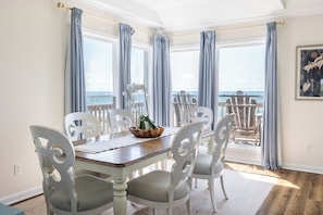 A dining area with a wooden table and white chairs, overlooking a balcony with a view of the ocean. - Ocean Reef 8-A2 | Oceanfront Condo (Emerald Isle)