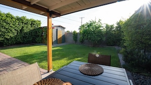 Un patio con mesa y sillas, un espacio cubierto y un césped cuidado.