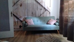 Ein Zimmer mit einer Couch, einer Holzwand, einem Teppich und einem Fenster mit Vorhängen.
