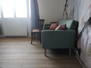 Ein Zimmer mit einem grünen Sofa, einem hölzernen Stuhl und einem Heizkörper an der Wand.