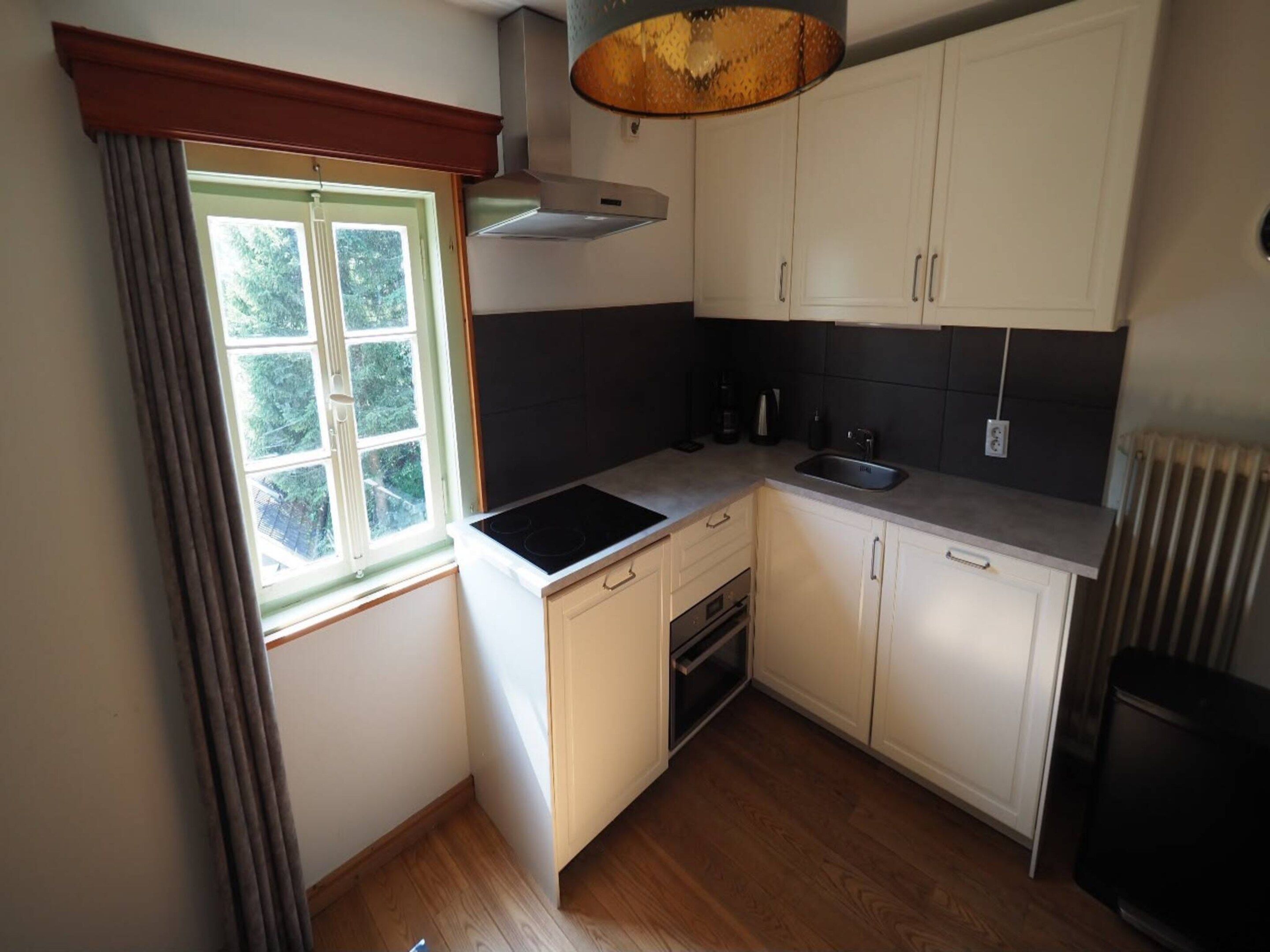 A compact kitchen with a window, a stove, a sink, and cabinets.