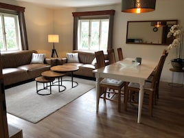 Una sala de estar moderna con un sofá, dos mesitas redondas, una mesa de comedor con sillas, una lámpara y una planta en maceta.