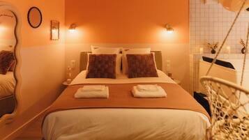 Een hotelkamer met een bed, twee kussens, een nachtkastje met een lamp, een spiegel en een wieg.