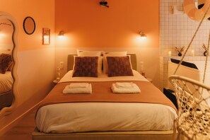 A hotel room with a bed, two pillows, a bedside table with a lamp, a mirror, and a crib. - La Pimenta – Escapade romantique & épicée (Dole)