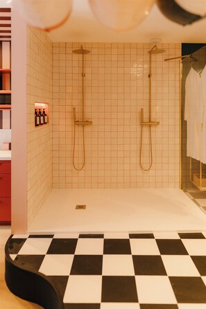 A bathroom with a checkered floor, two showerheads, and a towel rack with bottles. - La Pimenta – Escapade romantique & épicée (Dole)