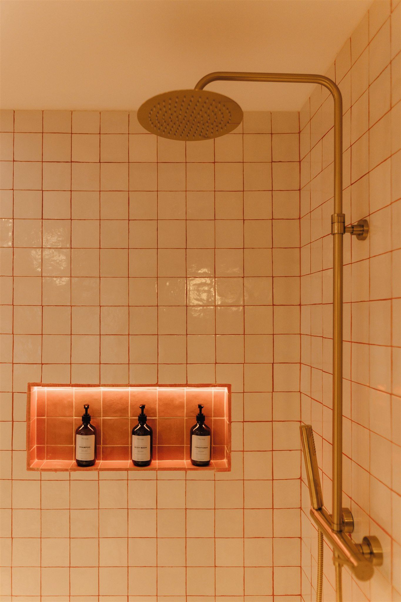 Een badkamer met een douche, betegelde wanden en drie flessen toiletartikelen op een plank.