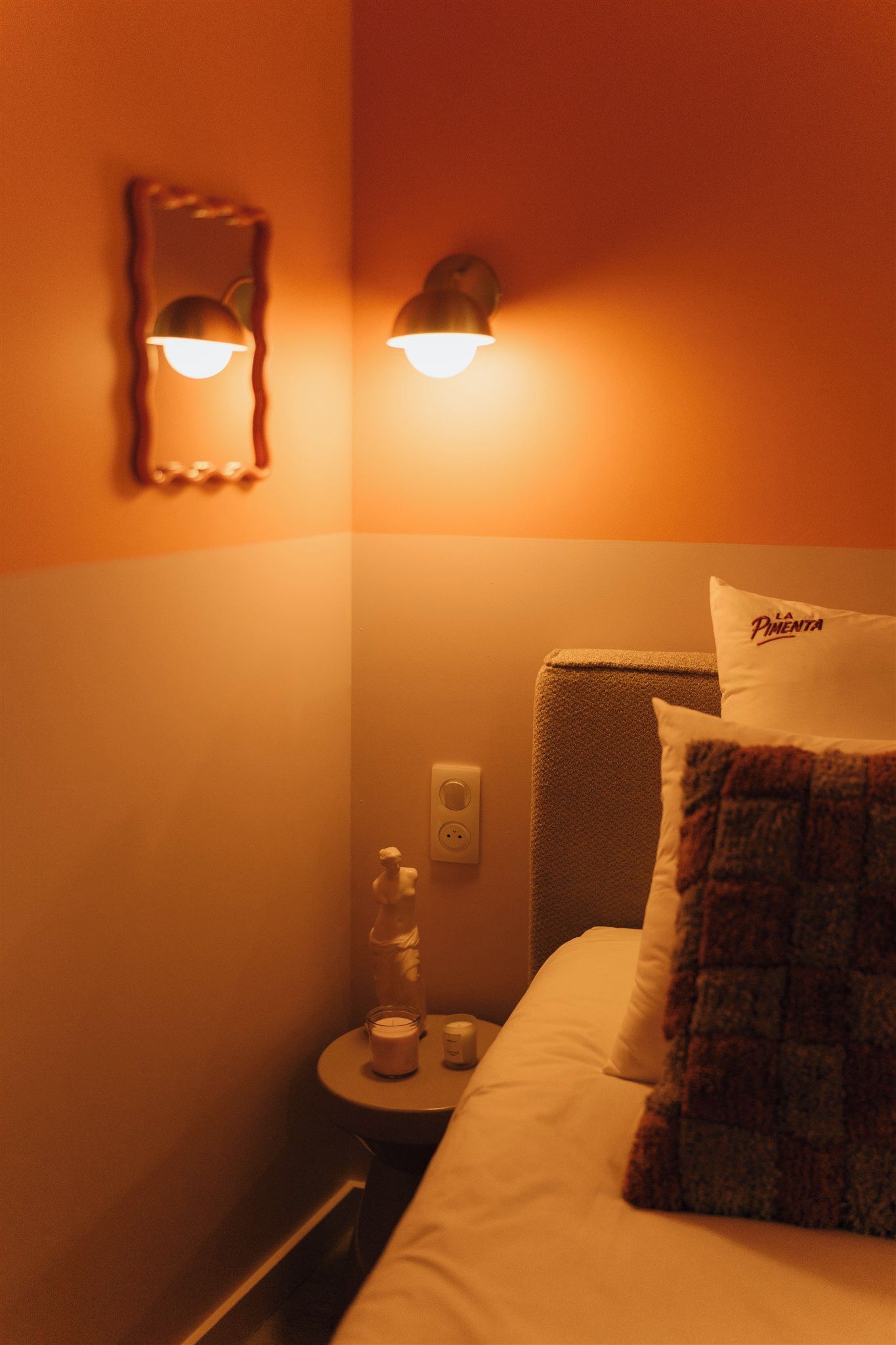 Une chambre d’hôtel comprenant un lit, une table de chevet, un luminaire fixé au mur et un objet décoratif.