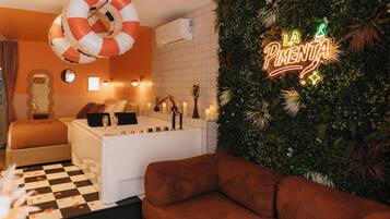 Een moderne hotelkamer met een geruit vloerkleed, een bruine bank, een witte badkuip en een neonbord aan de muur.