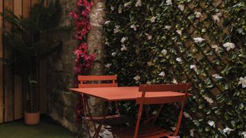 A red metal table and chair set against a wall covered in green foliage and pink flowers.