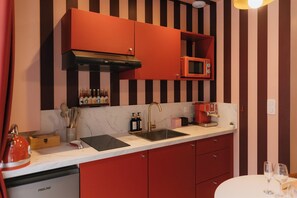 A kitchen with red cabinets, a stainless steel sink, and a microwave. - La Pimenta – Escapade romantique & épicée (Dole)