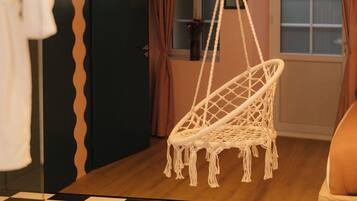 Une pièce avec un sol à carreaux, un fauteuil suspendu en macramé, un lit et une porte au motif ondulé.