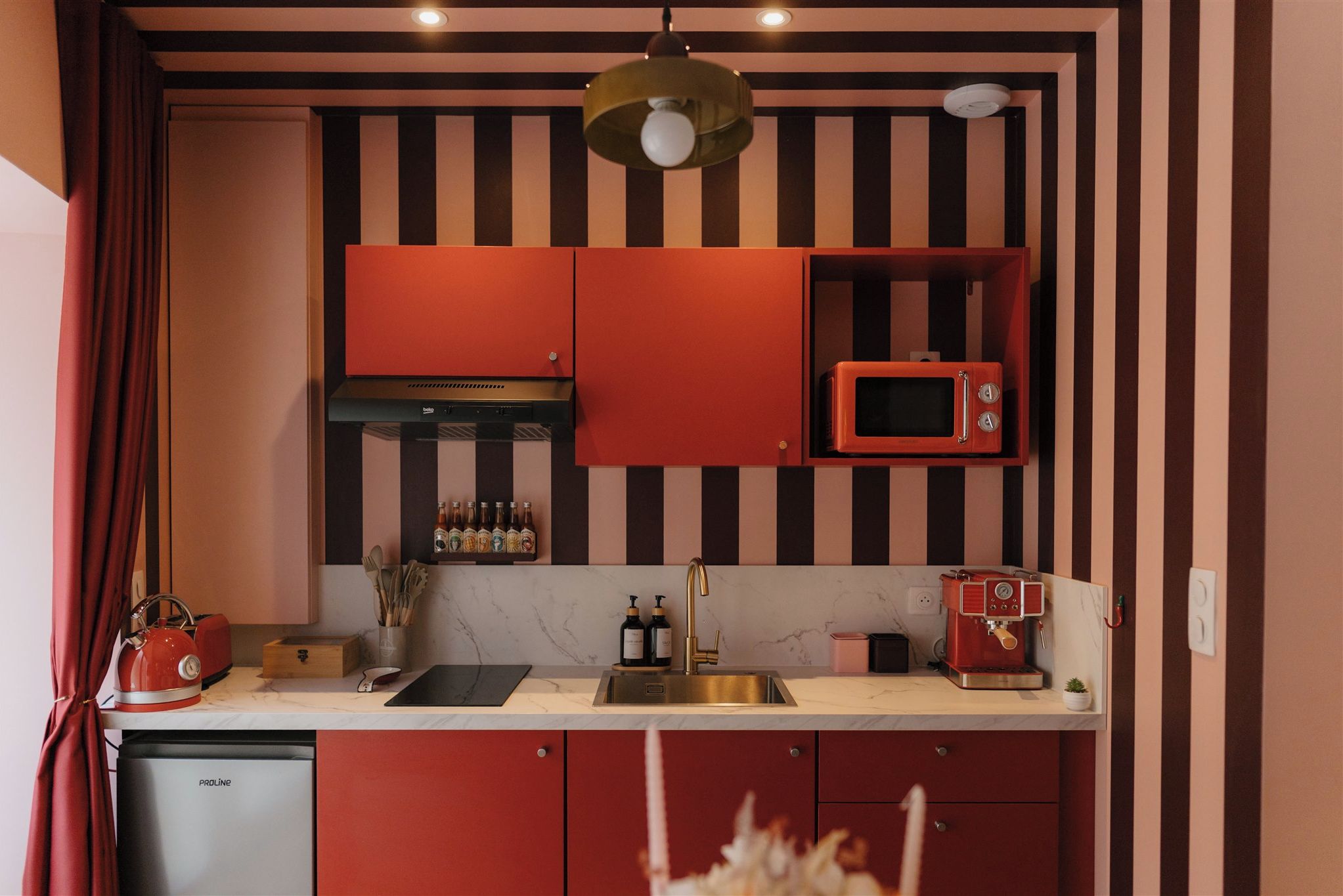 Une cuisine avec des placards rouges, un four à micro-ondes, une bouilloire et une machine à café.