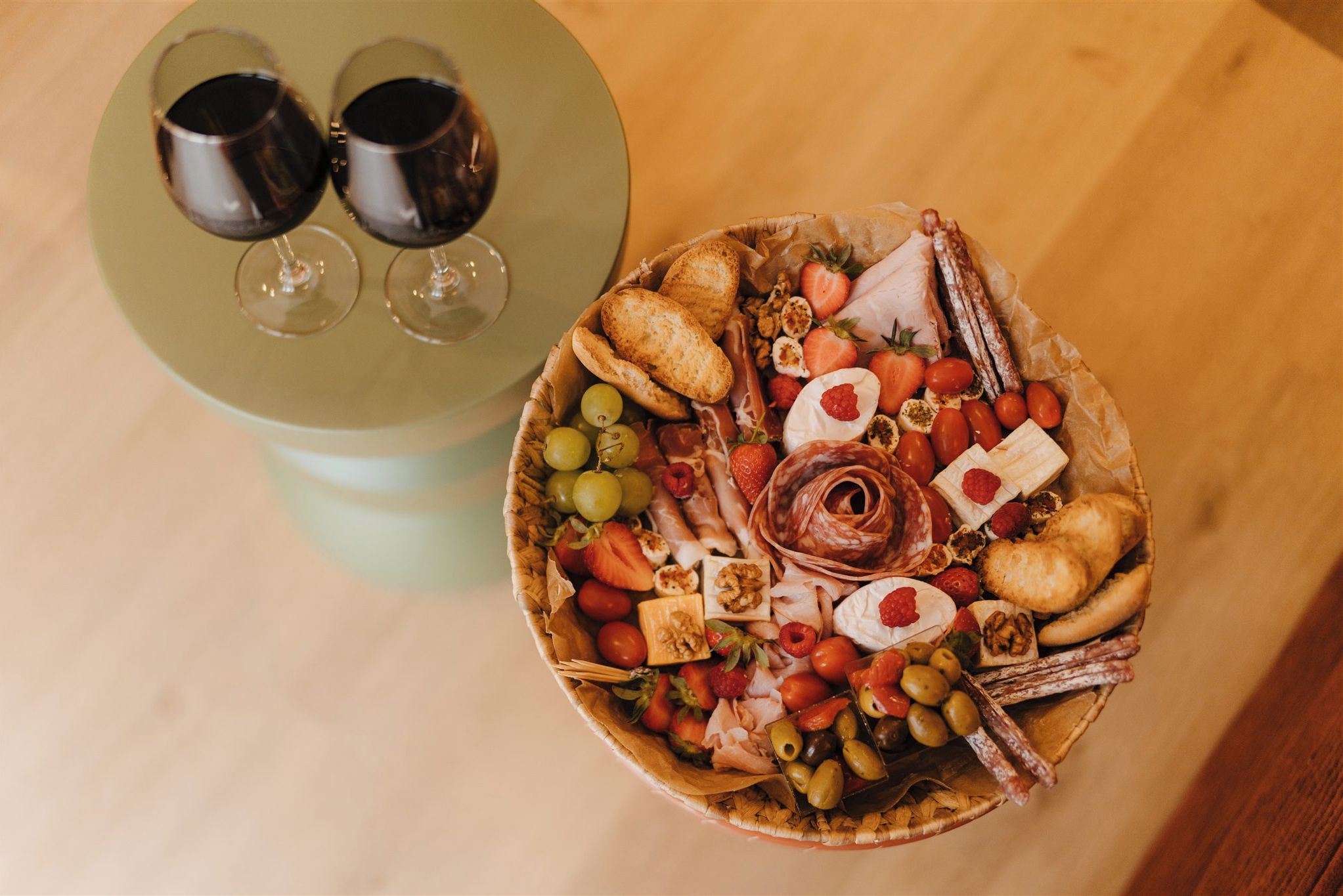 A charcuterie board with various cheeses, fruits, and nuts, accompanied by two wine glasses on a table.