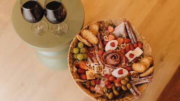 A charcuterie board with various cheeses, fruits, and nuts, accompanied by two wine glasses on a table.