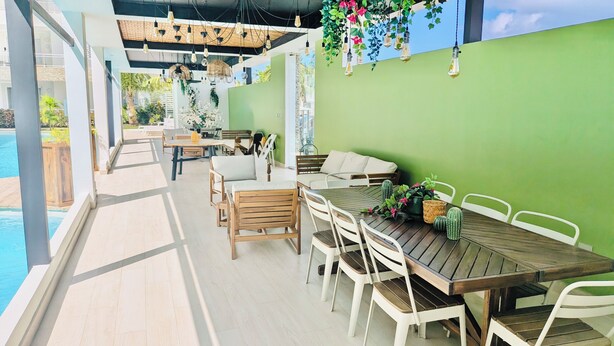 Een terras buiten met een zwembad, houten meubels en hangplanten.