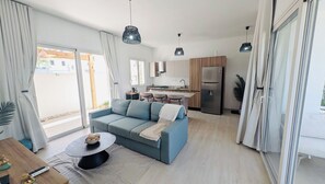 A modern living room with a sofa, a coffee table, and a kitchen area with a refrigerator and a sink.