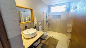 Een moderne badkamer met een grote spiegel, een rond wastafel, toilet en een douchecabine met glazen wanden.