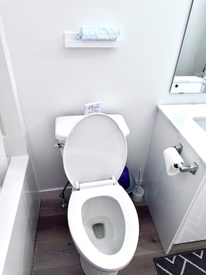 Une salle de bain moderne avec des toilettes blanches, un porte-rouleau de papier toilette et une brosse de toilette bleue.