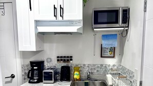 Une cuisine compacte avec des meubles blancs, un four à micro-ondes, une machine à café et un évier.