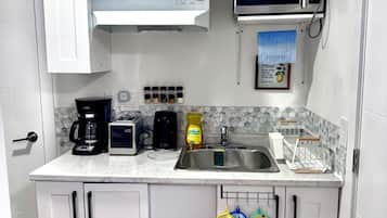 A kitchen with white cabinets, a microwave, a coffee maker, and a sink.