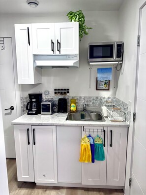 A compact kitchen with white cabinets, a microwave, a coffee maker, and a sink. - Cozy Central Winnipeg Main Floor Suite – Private & Quiet (Winnipeg)