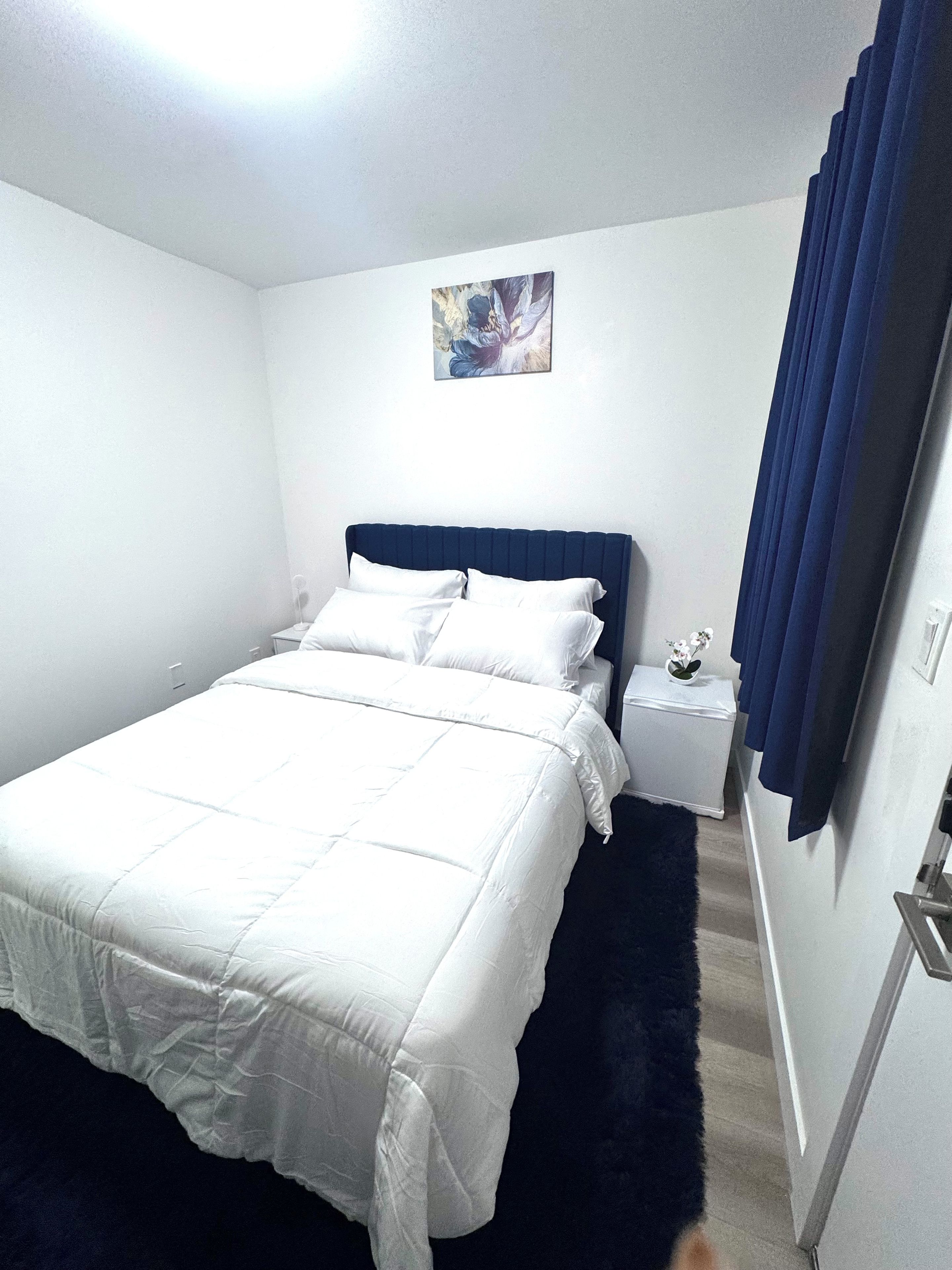 A hotel room with a bed, a nightstand, a painting on the wall, and a window with curtains.