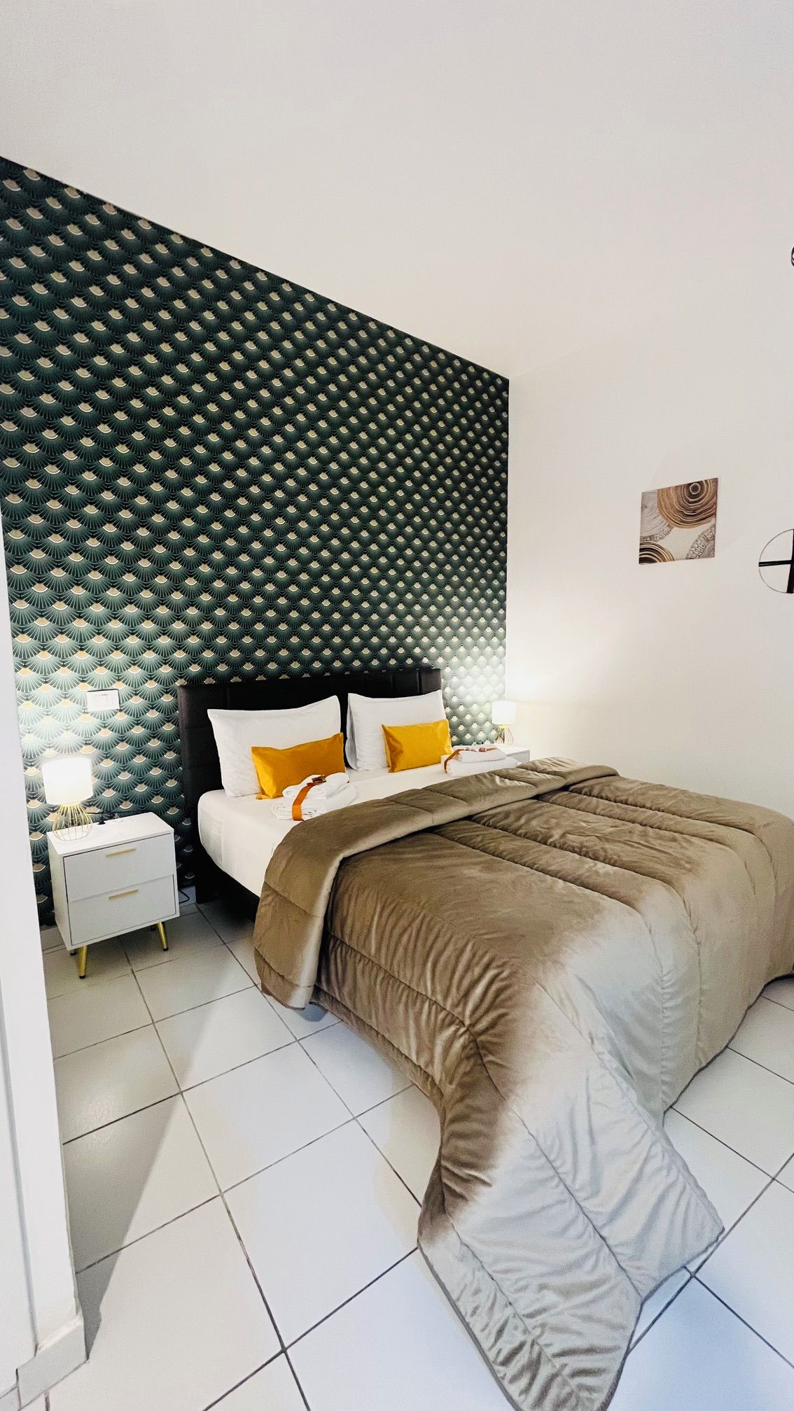 Une chambre à coucher avec une tête de lit à motifs, un lit recouvert d’une couverture marron, une table de chevet avec une lampe et une petite table de nuit.