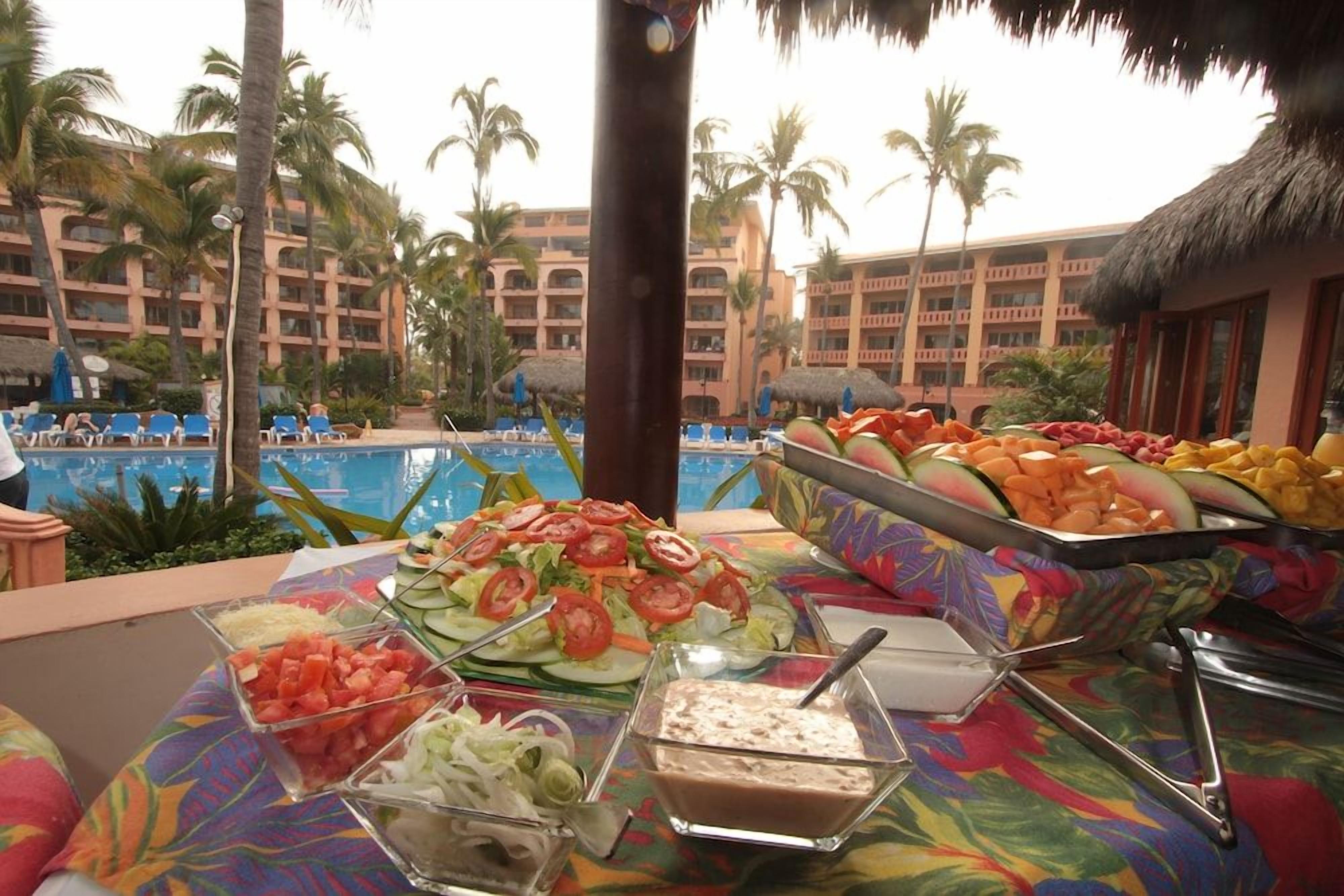 Una mesa de buffet con diversos alimentos y una zona de piscina al fondo.
