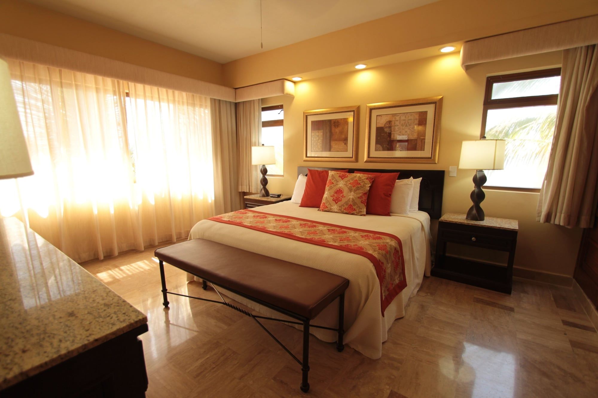 Una habitación de hotel con una cama, mesitas de noche, un banco y una ventana con cortinas.