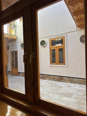 A view through a wooden-framed window with a white wall and a stone baseboard. - ANIS-PARI Hotel (Bukhara)