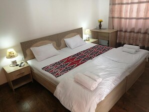 Ein ordentlich bezogenes Bett mit einem gemusterten Überwurf, ein Nachttisch mit Lampe und ein Beistelltisch mit Fernbedienung.