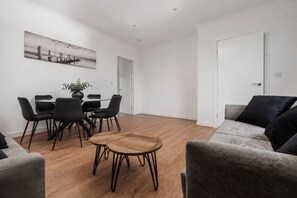 Ein modernes Wohnzimmer mit Essbereich, einem grauen Sofa und einem Holztisch.