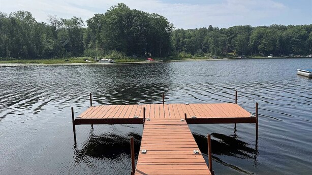 Une jetée en bois s’étendant dans un lac paisible, avec une rive boisée en arrière-plan.